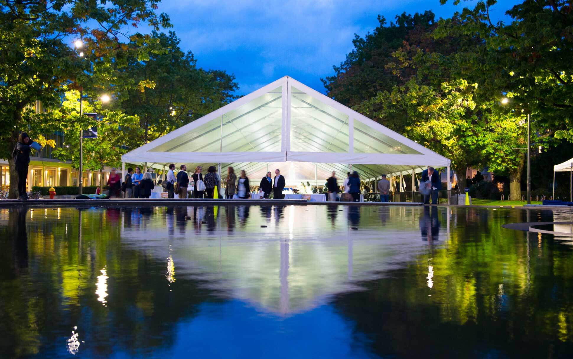 Visitors enjoy an evening event under a white tent along Main Mall at UBC Vancouver.
