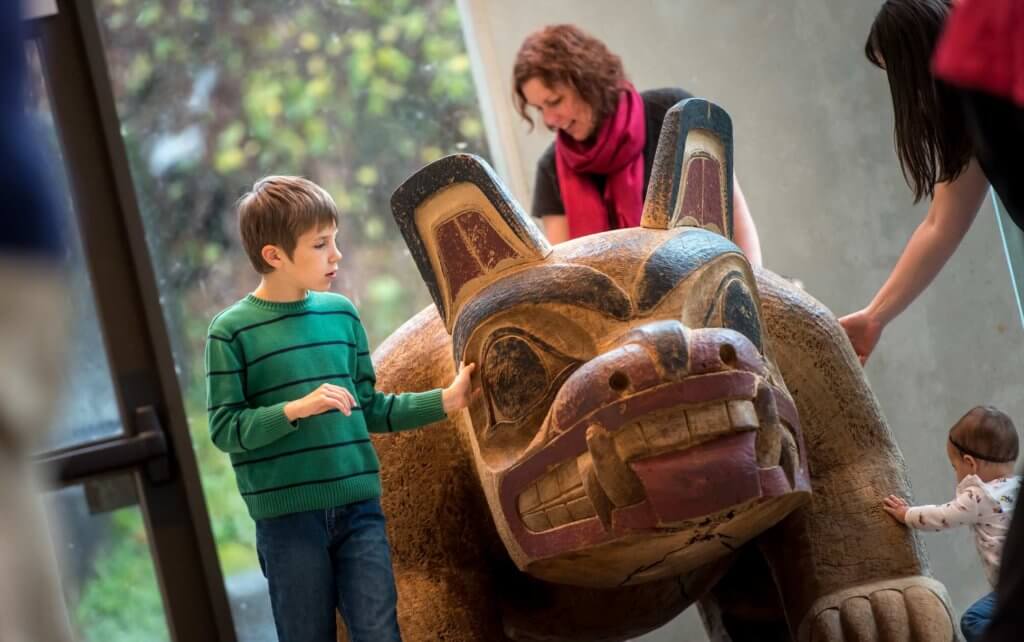 Children and adults touch a large Indigenous artwork at the Museum of Anthropology (MOA) at UBC Vancouver.